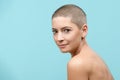 Studio headshot portrait of a beautiful young caucasian woman with shaved head against pastel blue background. Cancer survivor.