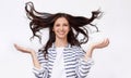 Studio image of beautiful young woman with flying hair smiling broadly and looking at he camera with raised hands, posing over Royalty Free Stock Photo