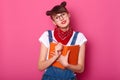 Studio image of cute female teenager with two funny bunches, holding diary and pensil in hands, looking directly at camera, writes Royalty Free Stock Photo