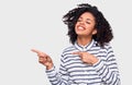 Studio image of happy African American young woman dressed in striped shirt, indicates aside with forefinger to blank copy space, Royalty Free Stock Photo