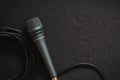 A studio microphone with black cable and black background behind