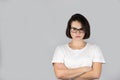 Studio photo on the background of a beautiful serious girl with dark hair in glasses with crossed hands on a white t-shirt Royalty Free Stock Photo