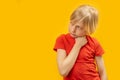 Studio photo of caucasian blonde boy in red T-shirt on yellow background. Brooding child looks to the side. Copy space