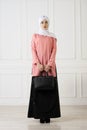 Studio photo girl with eastern appearance, in Muslim clothing with a scarf on her head and purse in hand, on a light classical bac Royalty Free Stock Photo