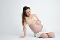 Studio photo of pregnant bunette woman in beige bra lies and looking at her tummy while touching it, copyspace for your Royalty Free Stock Photo