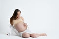 Studio photo of pregnant bunette woman in beige bra lies and looking at her tummy while touching it, copyspace for your Royalty Free Stock Photo