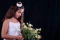 Studio photo of a pretty girl looking at a bouquet of daisy flowers on a dark background Royalty Free Stock Photo