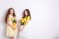 Studio photo of two standing smiling girls. A blond girl and a brunette girl hold vases with flowers. Brunette wears Royalty Free Stock Photo