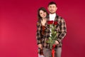 Studio photo. Young man with roses. The woman hugs him from behind. Red background. Side space Royalty Free Stock Photo