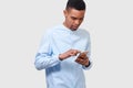 Studio portrait of African American young man holds modern smart phone, reading online news and blogging. Handsome Afro male Royalty Free Stock Photo