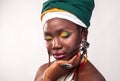 Studio portrait of African young woman with vibrant makeup of yellow and green colors. Colorful ethnic headwrap