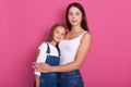 Studio portrait of attaractive young mother hugging her small daughter, females wearing white shirts and jeans, posing isolated Royalty Free Stock Photo