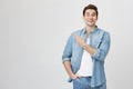 Studio portrait of attractive european man in denim glothes, pointing at upper left corner with index finger, expressing Royalty Free Stock Photo