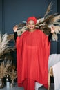 Studio portrait of an attractive happy African woman wearing traditional red clothing, headscarf and jewery standing