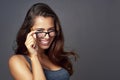 Heres lookin at you. Studio portrait of an attractive young woman peering over her glasses against a grey background. Royalty Free Stock Photo