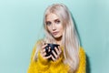 Studio portrait of beautiful blonde girl with blue eyes holding coffee black cup, wearing yellow sweater on aqua menthe background Royalty Free Stock Photo