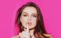 Studio portrait of beautiful elegant woman. Young lady showing shhh taboo sign with finger to lips over pink background Royalty Free Stock Photo