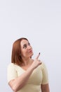 Studio portrait of a beautiful woman pointing her finger towards copy space and looking up on light background. Royalty Free Stock Photo