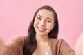 Studio portrait of beautiful woman smiling with white teeth and making selfie, photographing herself over pink background