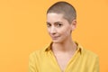 Studio portrait of a beautiful young caucasian woman with shaved head against bright yellow background. Cancer survivor portrait.