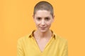 Studio portrait of a beautiful young caucasian woman with shaved head against bright yellow background. Cancer survivor portrait.