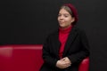 Studio portrait of a beautiful young girl in a beret and coat sitting on a red sofa on a black background Royalty Free Stock Photo