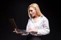 Studio portrait of blonde businesswoman in white blouse and black skirt holding laptop against dark background. Successful woman Royalty Free Stock Photo