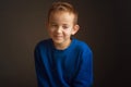 Studio portrait of boy in a blue classic sweater, sitting on a chair, looking away and smiling Royalty Free Stock Photo