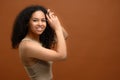 Studio portrait on the brown background of carefree serene multiracial woman looking at camera and laughs