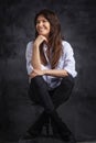 Studio portrait of a brunette haired attractive woman wearing white shirt and black jeans while posing at isolated dark background Royalty Free Stock Photo