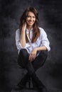 Studio portrait of a brunette haired attractive woman wearing white shirt and black jeans while posing at isolated dark background Royalty Free Stock Photo