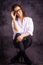 Studio portrait of a brunette haired attractive woman wearing white shirt and black jeans while posing at isolated dark background Royalty Free Stock Photo