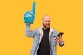 Cheerful bearded bald man wearing foam finger glove and looking at the phone. Royalty Free Stock Photo