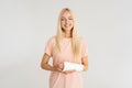 Studio portrait of cheerful blonde young woman with broken arm wrapped in plaster bandage smiling looking at camera Royalty Free Stock Photo