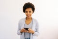 Studio portrait of cheerful curly African American young woman using smartphone typing browsing looking to device screen Royalty Free Stock Photo