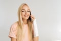 Studio portrait of cheerful injured blonde young woman with broken arm wrapped in plaster bandage talking smartphone on