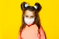 Studio portrait of child girl wearing medical mask on yellow background. Prevention of coronavirus and covid-19. Royalty Free Stock Photo