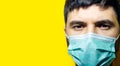 Studio portrait, close-up portrait of young sick man wearing medical flu mask on yellow background with copy space. Royalty Free Stock Photo