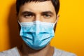 Studio portrait, close-up portrait of young sick man wearing medical flu mask on yellow background with copy space. Royalty Free Stock Photo