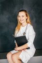 Studio portrait concept of a beautiful fashionable blonde female doctor in a white uniform on a black background with a folder in Royalty Free Stock Photo