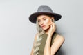 Studio portrait of cute blonde girl touching wireless earphones while listening to music, on white background. Wearing grey hat Royalty Free Stock Photo