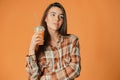 Cute caucasian young brunette girl holding plastic cup of orange juice on orange background Royalty Free Stock Photo