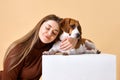 Studio portrait of dog and owner. Young woman smiling and hugging her favorite puppy Beagle dog against beige background Royalty Free Stock Photo
