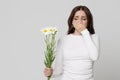 Studio portrait of female covering her nose, having an allergic reaction to flowers - chamomile, isolated. Allergy concept Royalty Free Stock Photo