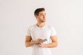 Studio portrait of focused young man holding in hands paper book on white  background in studio, looking away. Royalty Free Stock Photo