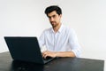 Studio portrait of friendly young man in shirt working on laptop computer, typing on keyboard, looking at camera sitting Royalty Free Stock Photo