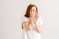 Studio portrait of frightened redhead young woman looking shy or terrified covering hiding face with hands peeping