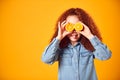 Studio Portrait Of Girl Holding Two Orange Halves In Front Of Eyes Against Yellow Background Royalty Free Stock Photo