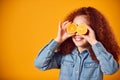 Studio Portrait Of Girl Holding Two Orange Halves  in Front Of Eyes Against Yellow Background Royalty Free Stock Photo