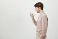 Studio portrait of handsome adult man standing in profile, holding smartphone and talking to personal assistant or while Royalty Free Stock Photo